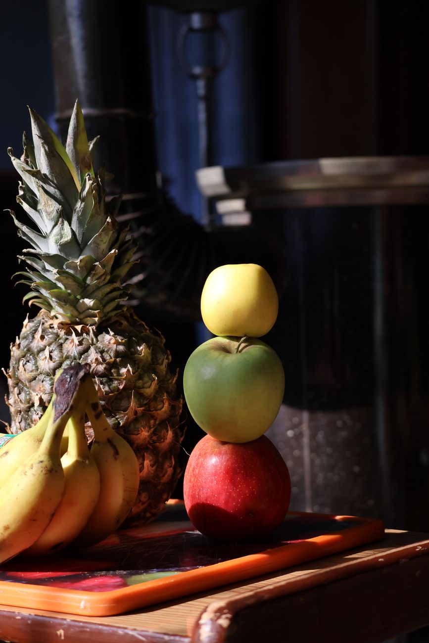 A vibrant stack of fruits including apples, bananas, and pineapple under warm lighting.