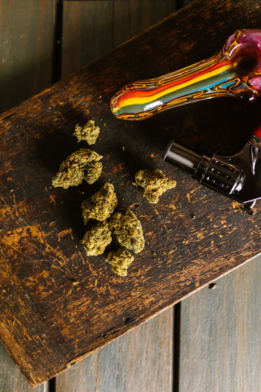 A colorful glass pipe and cannabis buds placed on a rustic wooden table in a vertical shot.