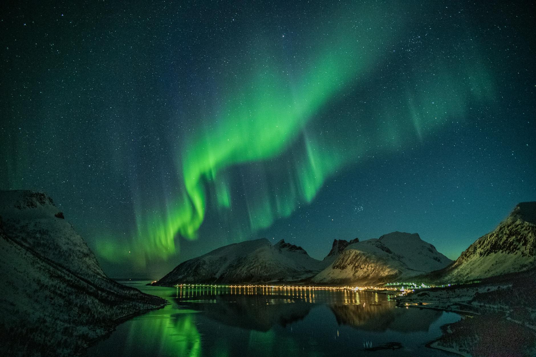 Mesmerizing northern lights illuminating snowy mountains and reflecting on a tranquil lake under a starry night sky.